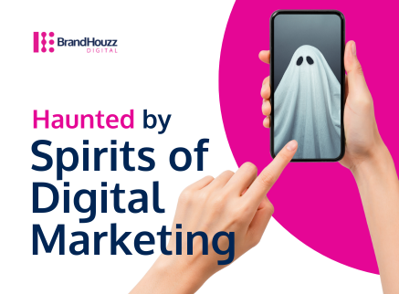 BrandHouzz Digital graphic with a Halloween theme titled 'Haunted by Spirits of Digital Marketing.' The image shows a hand pointing to a smartphone screen with a cartoon ghost on it, set against a white and pink background.